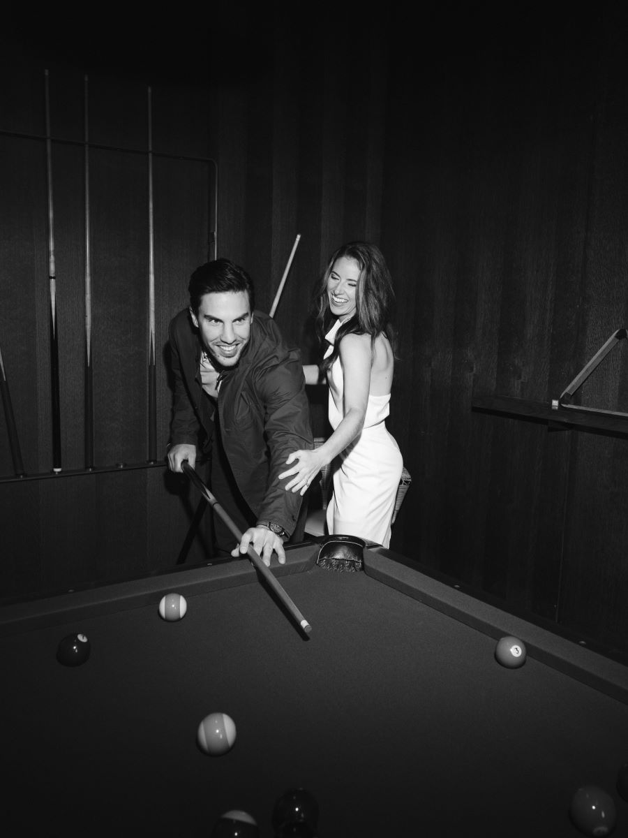 A couple playing pool together and laughing theya re both holding pool sticks 