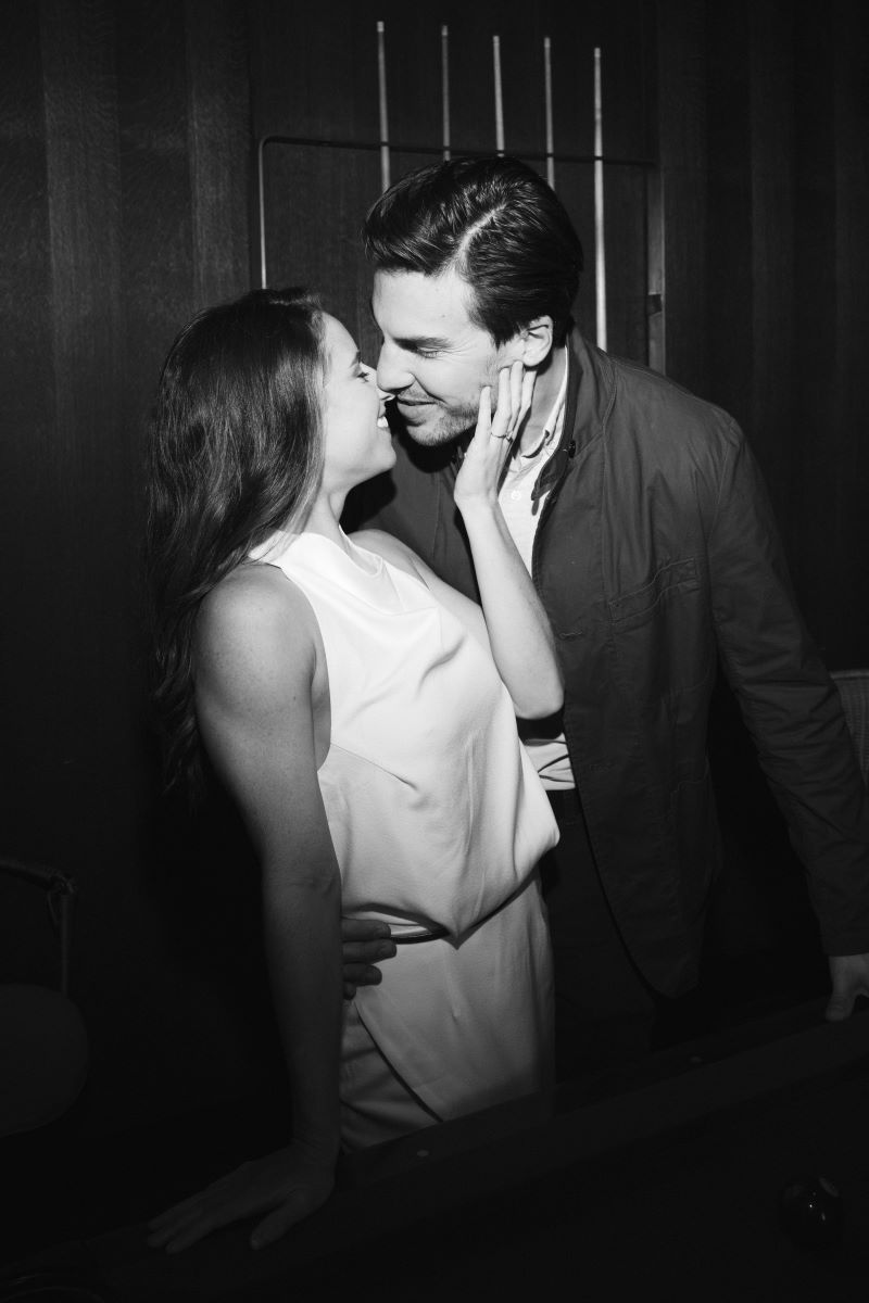 A couple leaning toward each other about to kiss the woman is waring a white dress and her partner is grabbing her around the waist they are both smiling at each other 