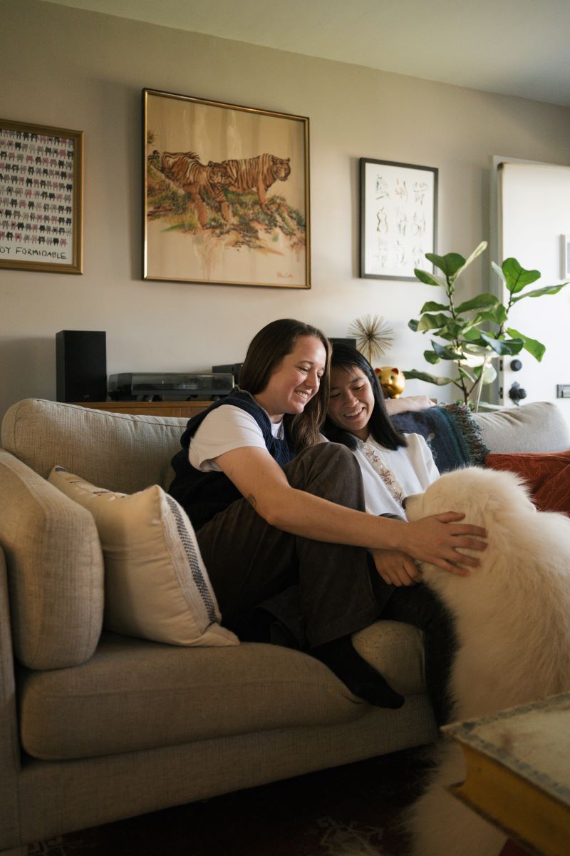 A couple sitting on their couch together petting and looking at their dog 