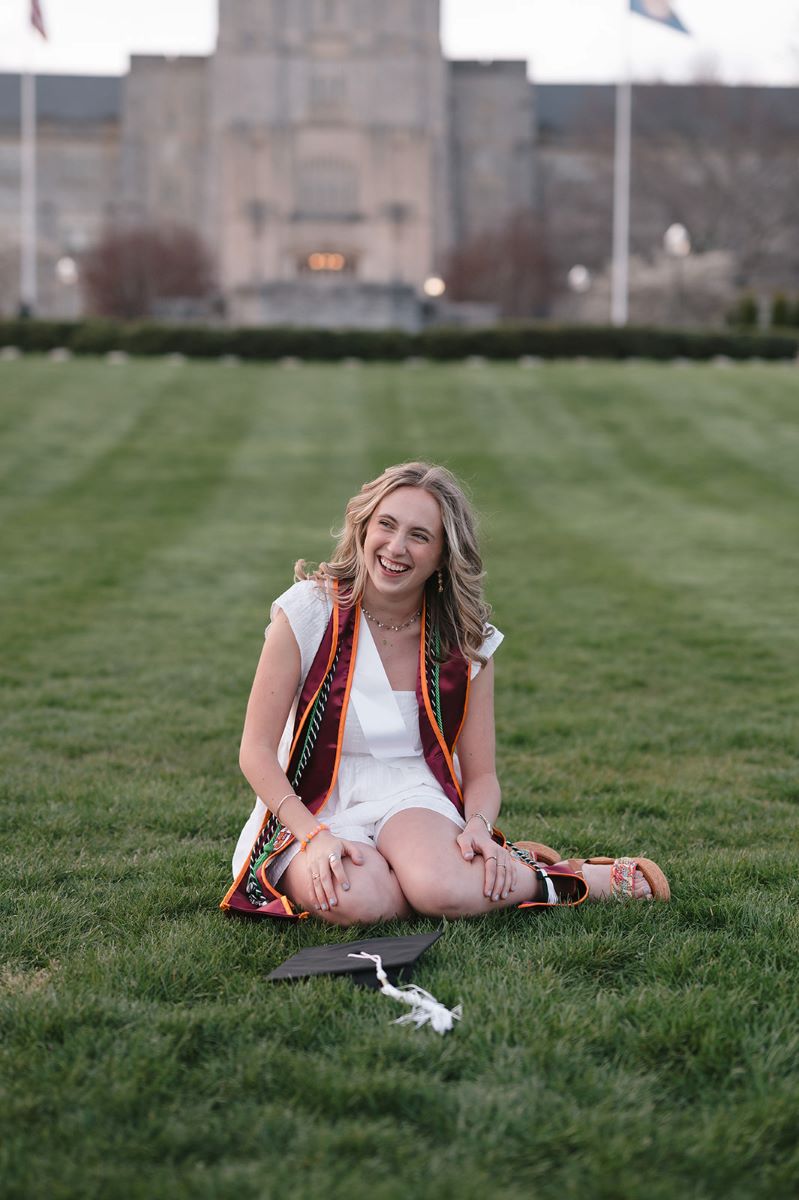 A girl sitting on a lawn laughing with her graduation cap in front on her 